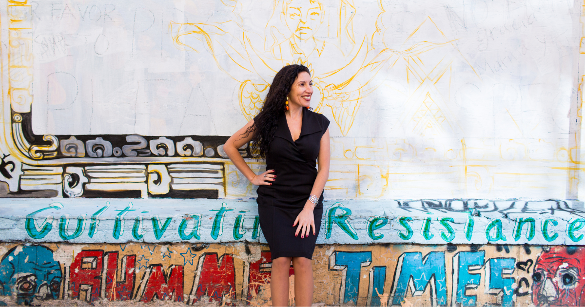 Maritza Schafer in a black dress smiling in front of a vibrant graffiti mural wall